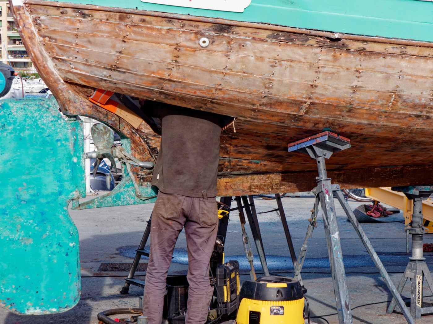 A wooden boat resting on stands in a working yard
