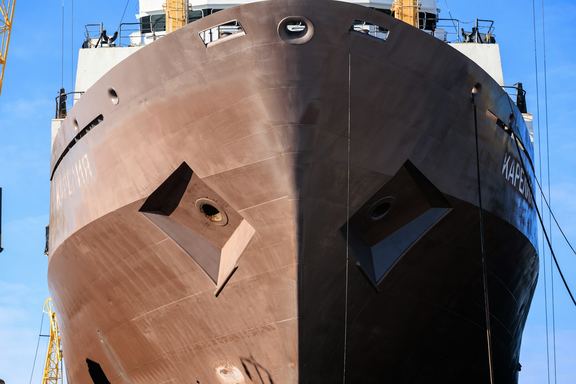 The bow of a large vessel rising above a dry dock against a clear sky