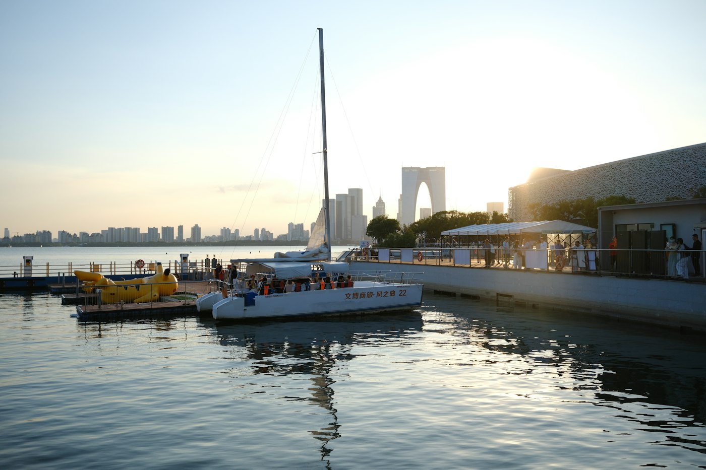 A white catamaran docked at a pier with a city skyline behind