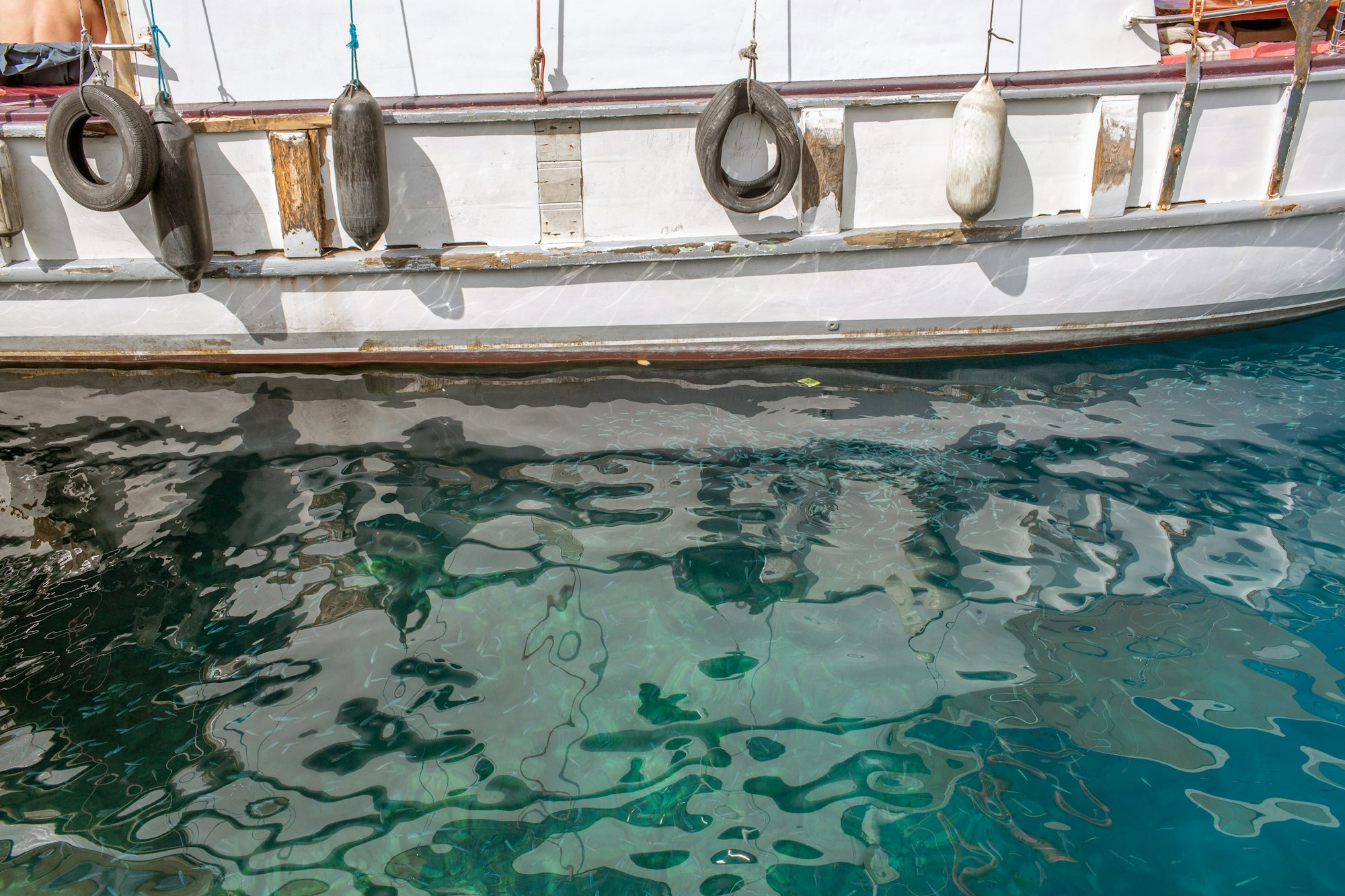 Weathered white boat hull with hanging fenders above clear water