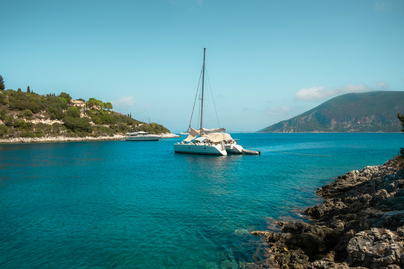 A catamaran in clear blue water beside a rocky shore